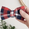 A hand holding a red, white, and blue plaid bow tie against a white background.