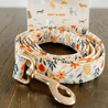A floral-patterned dog leash with a metal buckle, placed on a wooden surface.