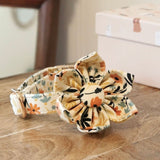 A floral print bow tie is displayed on a wooden surface, with a wooden chair and a box with a floral pattern in the background.