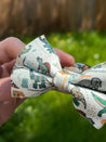 A hand is holding a bow tie with a dinosaur print pattern.