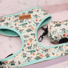 A white and teal dog harness with a dinosaur print pattern, featuring various dinosaur illustrations such as T-Rexes, Velociraptors, and Stegosaurus. The harness appears to be a pet product, possibly designed for a young dog or a child.