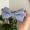 A hand is holding a blue and white striped bow tie against a white wall background.